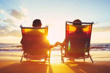 Pension contributions taxation - Tax Benefits - image of the beach with the sun setting in the background, two people sat on deckchairs holding hands